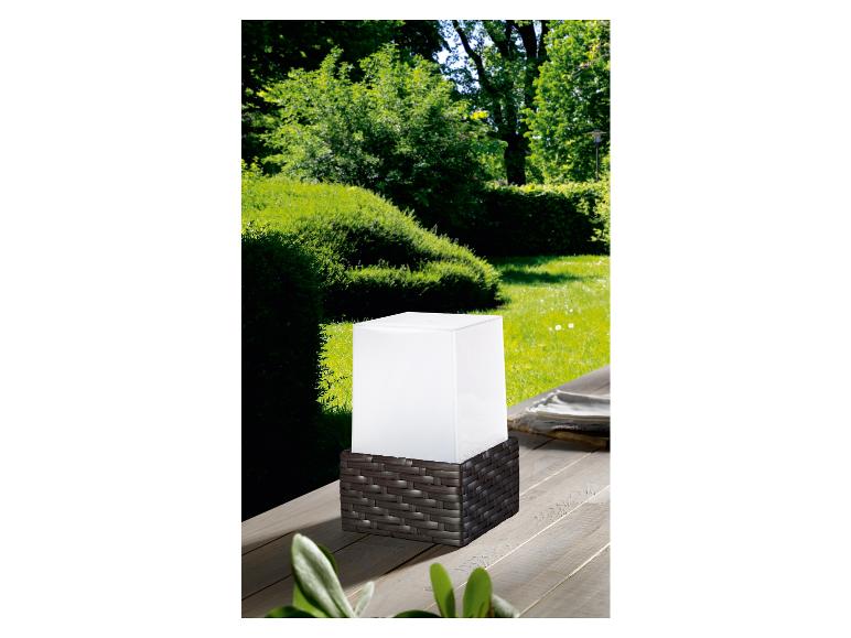 Een witte buitenlamp met een rotan basis op een houten terras.
